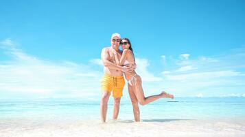 Una pareja abrazándose en una playa con cielos despejados y aguas tranquilas.