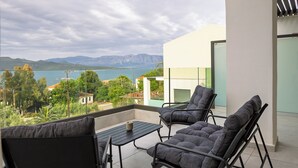 Ein Balkon mit zwei gepolsterten Stühlen und einem kleinen Tisch, mit Blick auf eine malerische Berg- und Wasserlandschaft.
