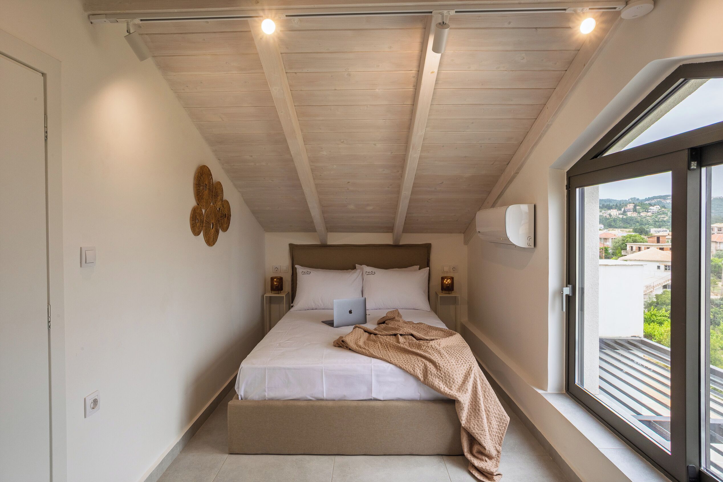 A bedroom with a bed, a laptop, a window with a view, and a ceiling light.