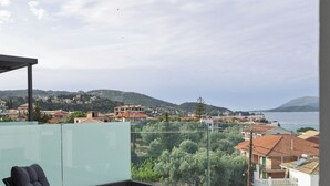 Ein Balkon mit Blick auf eine Küstenstadt, ausgestattet mit zwei Stühlen und einem Tisch, auf dem ein Buch liegt.
