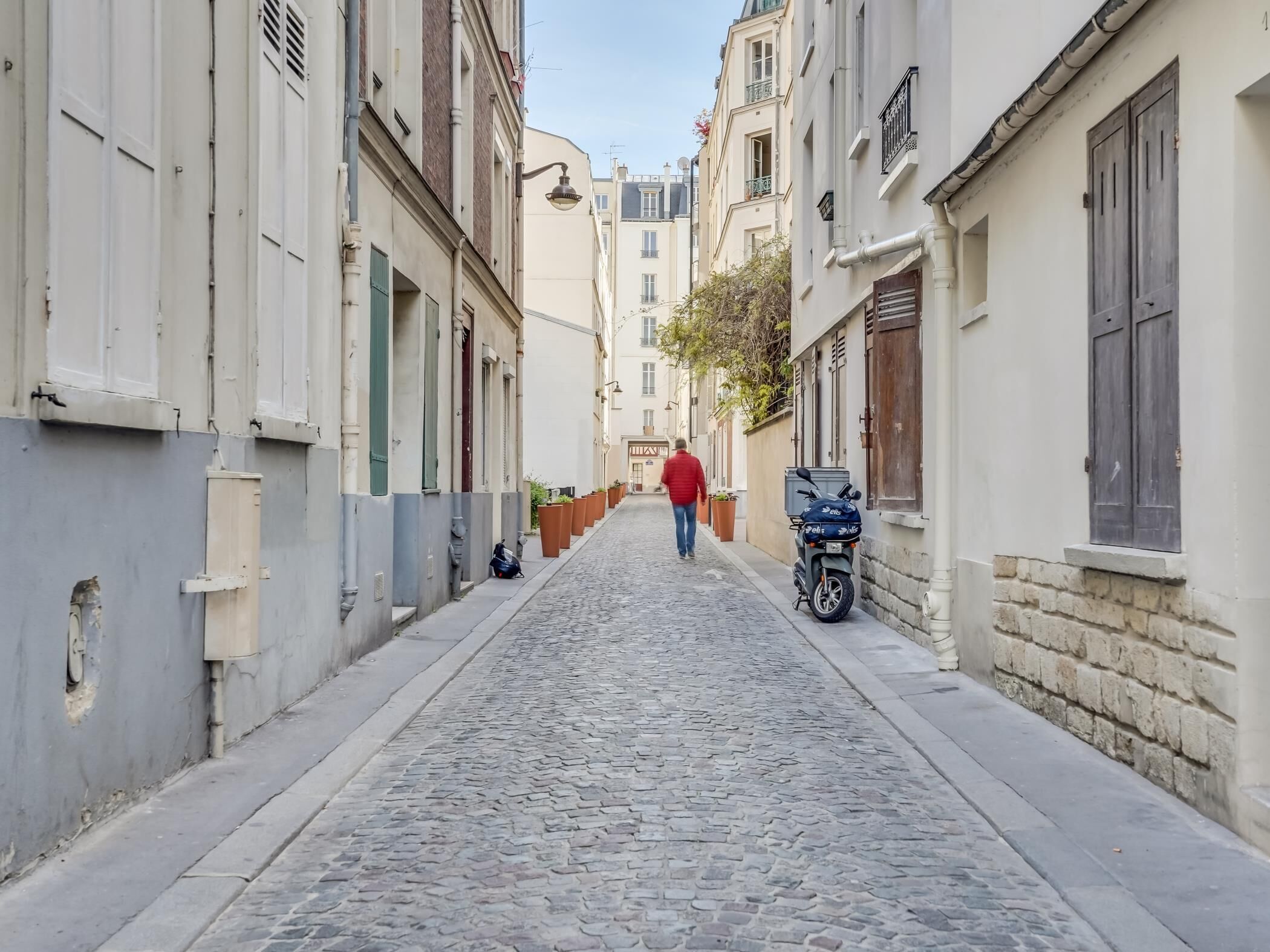 A narrow cobblestone street flanked by buildings with traditional European architecture, including shutters and balconies.