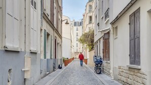A narrow cobblestone street flanked by buildings with traditional European architecture, including shutters and balconies.