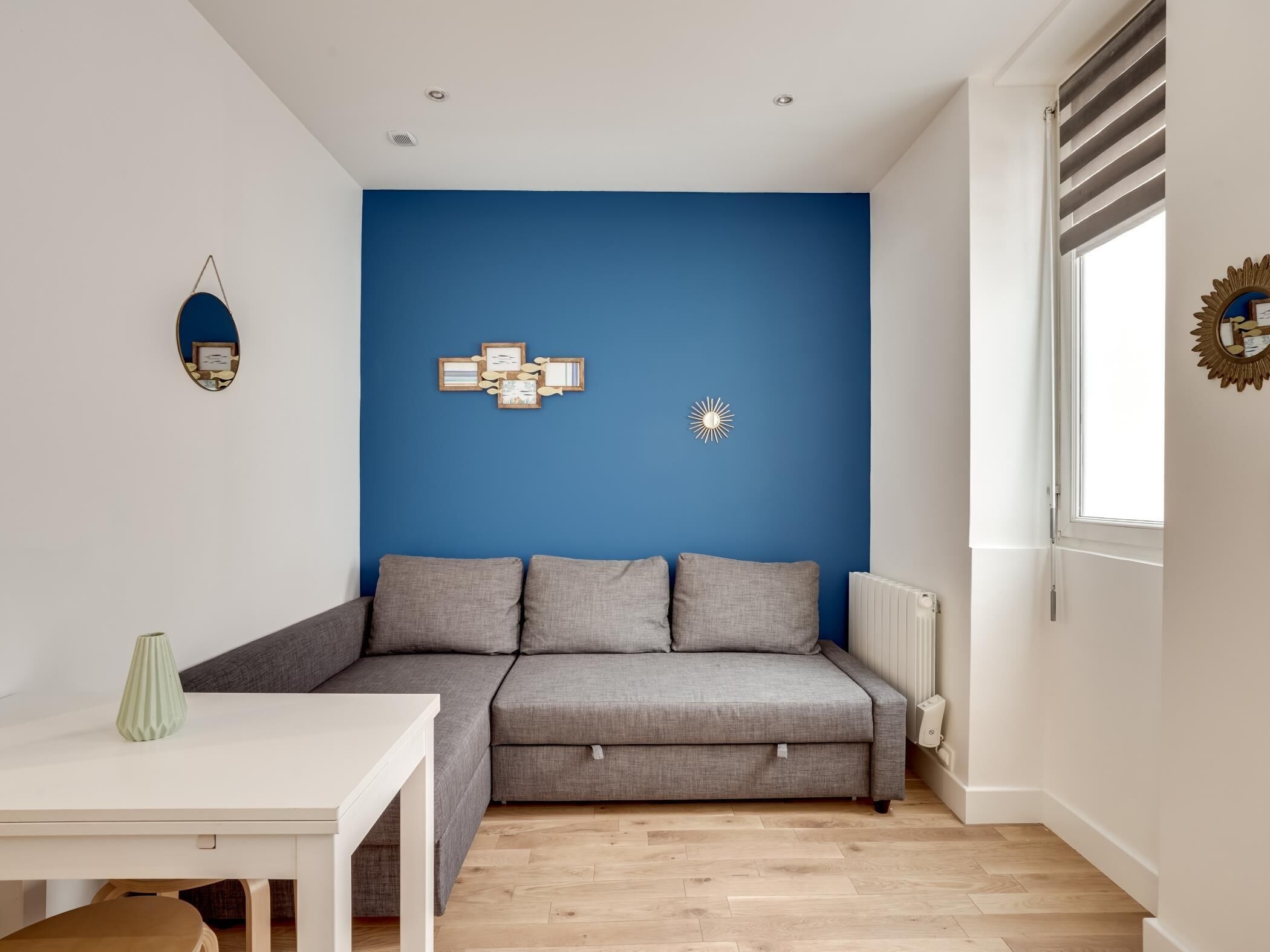 Un salon moderne avec un canapé gris, une table blanche et un mur d’accent bleu.