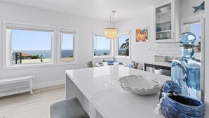 A modern kitchen with large windows, a central island, and a view of the ocean. - Penthouse! Steps from Victoria Beach, 180 degree ocean views! (Laguna Beach)