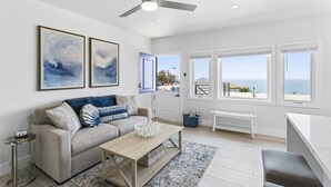 A spacious living room with a sofa, coffee table, and a view of the sea through large windows. - Penthouse! Steps from Victoria Beach, 180 degree ocean views! (Laguna Beach)