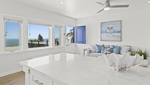 A modern kitchen with a large island, white cabinetry, and a view of the ocean.