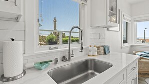 A modern kitchen with a large window, stainless steel sink, and white cabinetry.