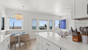 A modern kitchen with white cabinetry, a marble countertop, and a view of the ocean.