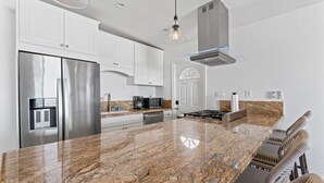 A modern kitchen with white cabinets, stainless steel appliances, a granite countertop, and a built-in gas stove. - Private beach, toes on the Sand!  Waterworld! STR23-0121 (Dana Point)