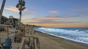 A beach with a wooden deck, palm trees, and a view of the ocean. - Private beach, toes on the Sand!  Waterworld! STR23-0121 (Dana Point)