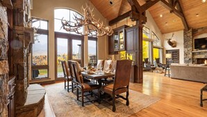 Un vaste espace dédié à la salle à manger, avec une grande table en bois, une cheminée en pierre et une vue sur l’extérieur.
