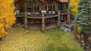 Une grande cabane rustique en rondins de bois, à plusieurs niveaux, dotée de grandes fenêtres et d’un espace extérieur aménagé avec des sièges.