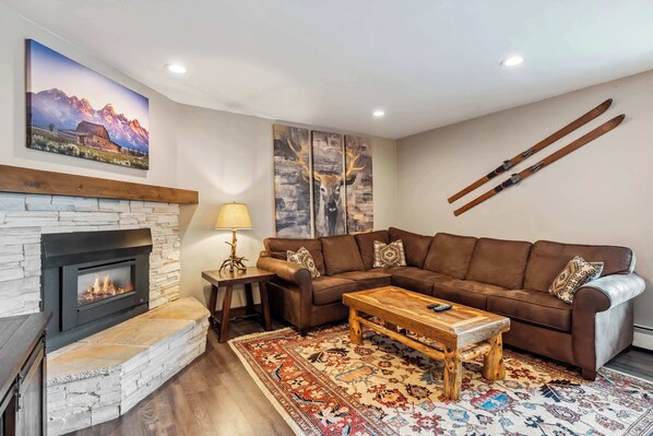 A cozy living room with a fireplace, a brown leather sofa, a wooden coffee table, and a patterned rug.