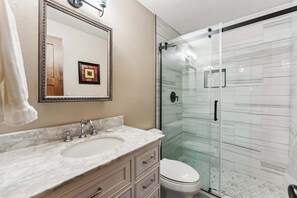 A bathroom with a marble sink, a framed mirror, a toilet, and a glass-enclosed shower.