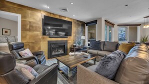 A modern living room with leather sofas, a fireplace, a flat-screen TV, and a large window.
