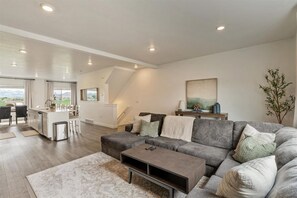 A spacious living area with a grey sofa, a coffee table, and a dining area with a kitchen in the background.