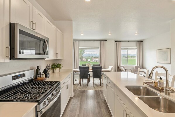 A modern kitchen with stainless steel appliances, a dining area with a view, and a large island with a sink.
