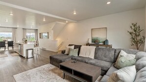 A spacious living area with a grey sofa, a coffee table, and a dining area with a kitchen in the background.
