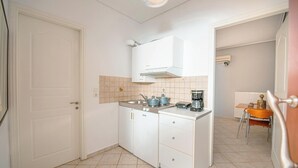 A compact kitchen with white cabinets, a stove, and a coffee maker. - OLIA  APARTMENTS LYGIA (Lefkada)