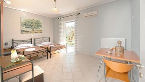 A modern bedroom with a bed, bedside table, and a desk with a chair. There is a window with curtains, an air conditioning unit, and a painting on the wall. - OLIA  APARTMENTS LYGIA (Lefkada)