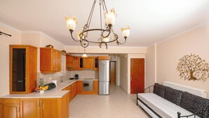 A compact kitchen with wooden cabinets, a stainless steel refrigerator, and a chandelier. - OLIA  APARTMENTS LYGIA (Lefkada)