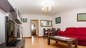 Una sala de estar moderna con un televisor de pantalla plana, un sofá rojo, una mesa de centro de madera y un comedor con una mesa y sillas.