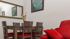 Un comedor con una mesa y sillas de madera, un jarrón con flores secas y un sofá rojo.