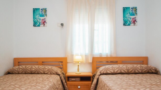Habitación doble con dos camas, una mesita de noche con lámpara y dos cuadros colgados en la pared.