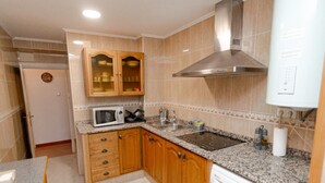 Una cocina compacta con armarios de madera, un microondas, un lavamanos y una lavadora integrada.