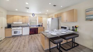 A modern kitchen with wooden cabinets, a granite countertop, a built-in oven, and a refrigerator. - Relaxing Coastal Cottage Close to the Beach (Galveston)