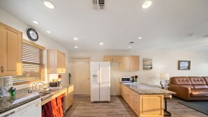 A modern kitchen with wooden cabinets, a built-in refrigerator, a microwave, and a dining area with a table and chairs. - Relaxing Coastal Cottage Close to the Beach (Galveston)