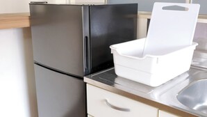 Una cocina con un refrigerador negro, una encimera blanca y un caja de almacenamiento blanca.