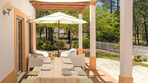 An outdoor patio with a table set for dining, surrounded by white chairs and a large umbrella.