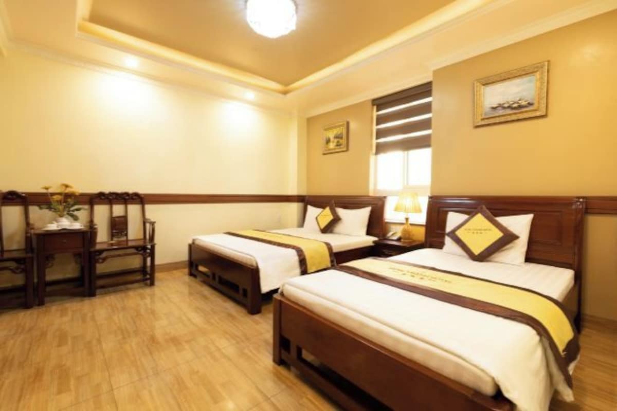 A hotel room with two beds, wooden headboards, a nightstand, a lamp, and a small table with a vase.