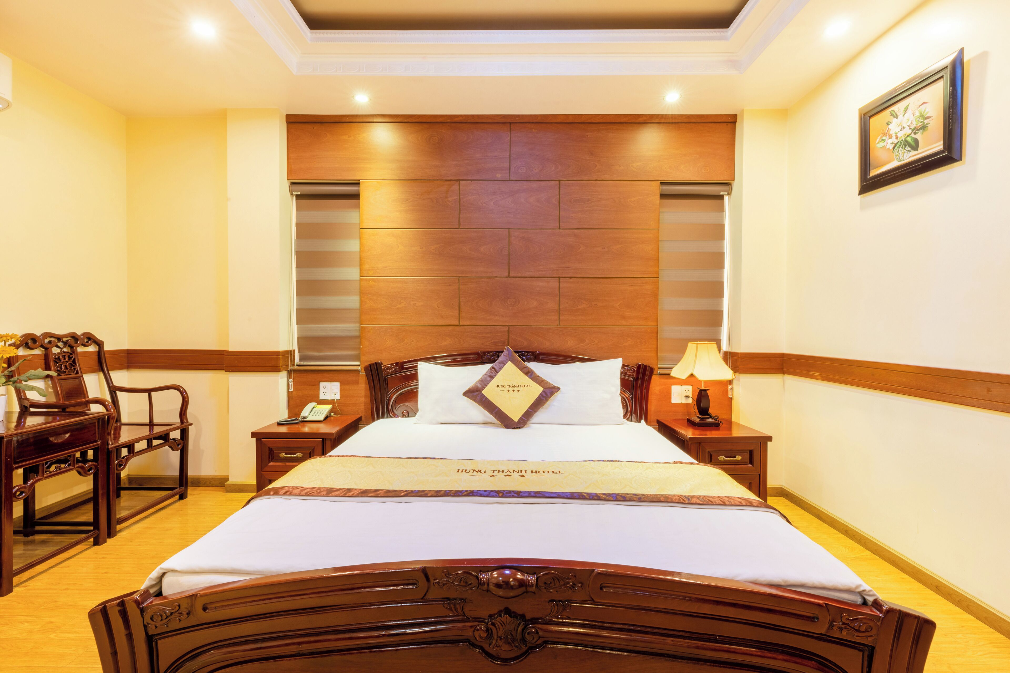Une chambre d’hôtel avec un grand lit, une tête de lit en bois, des tables de chevet, un bureau et une chaise.