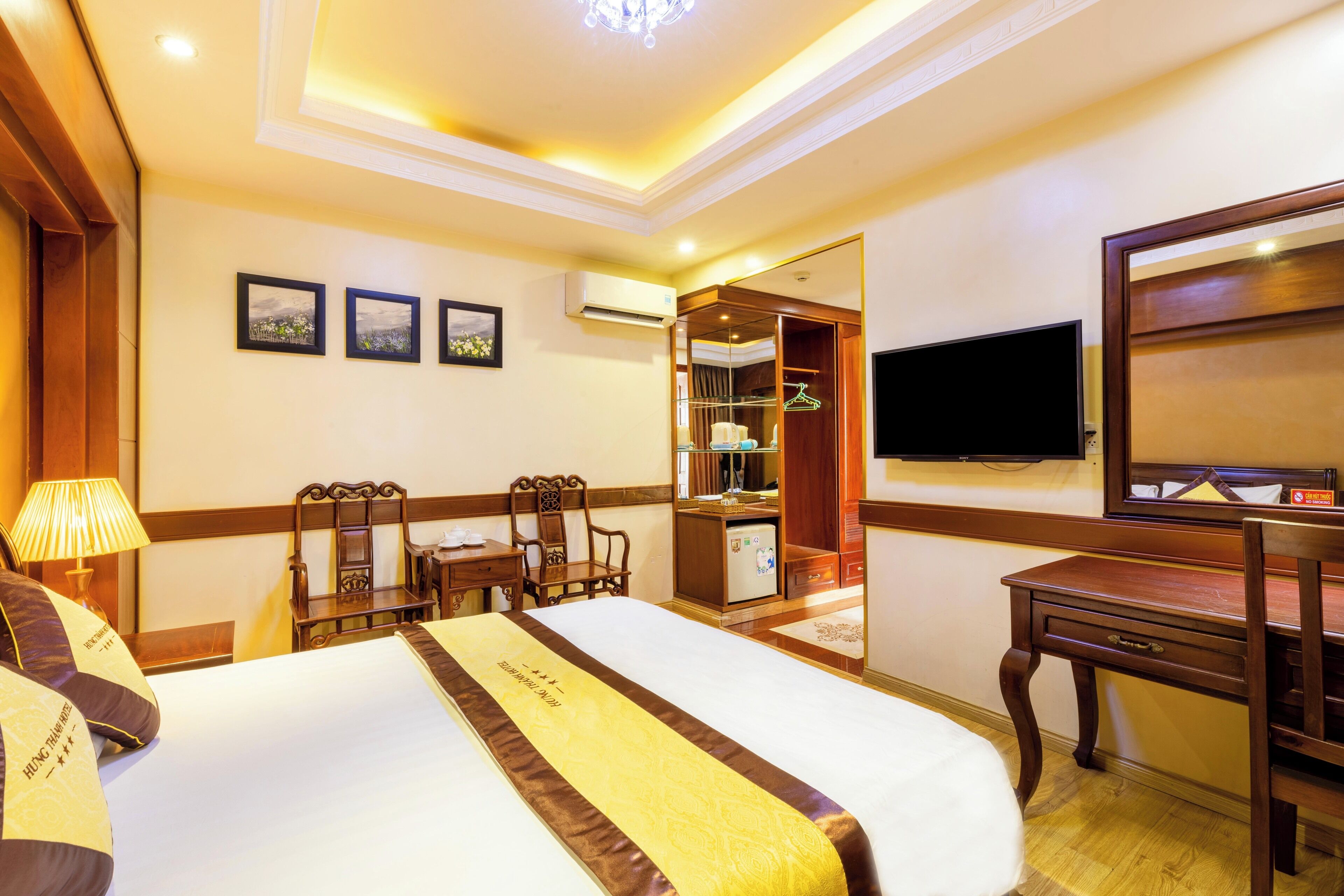 A hotel room with a large bed, a desk with a chair, a television, and a wardrobe.