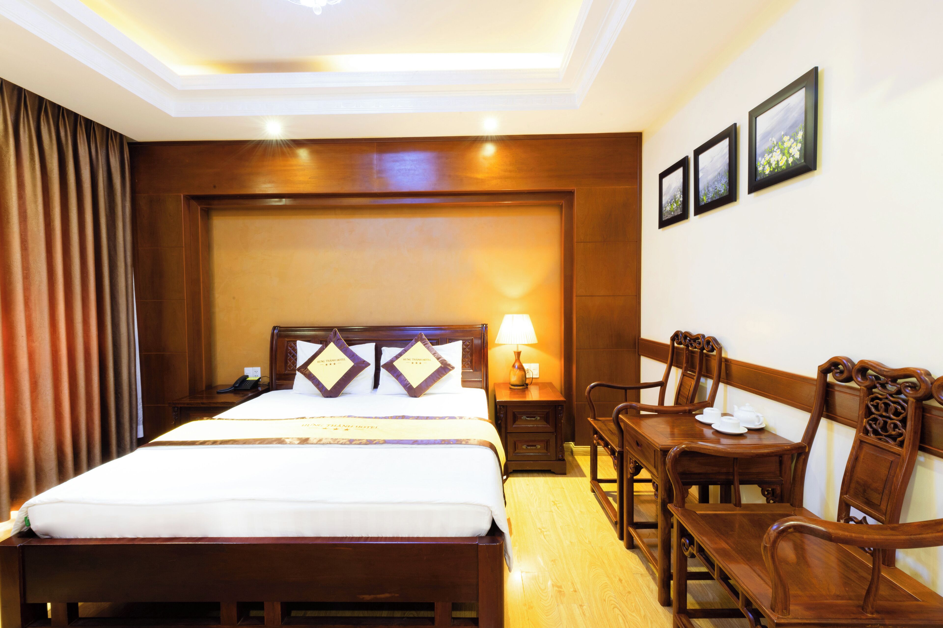 Une chambre d’hôtel avec un grand lit, une tête de lit en bois, une table de chevet, une lampe et une table à manger avec des chaises.