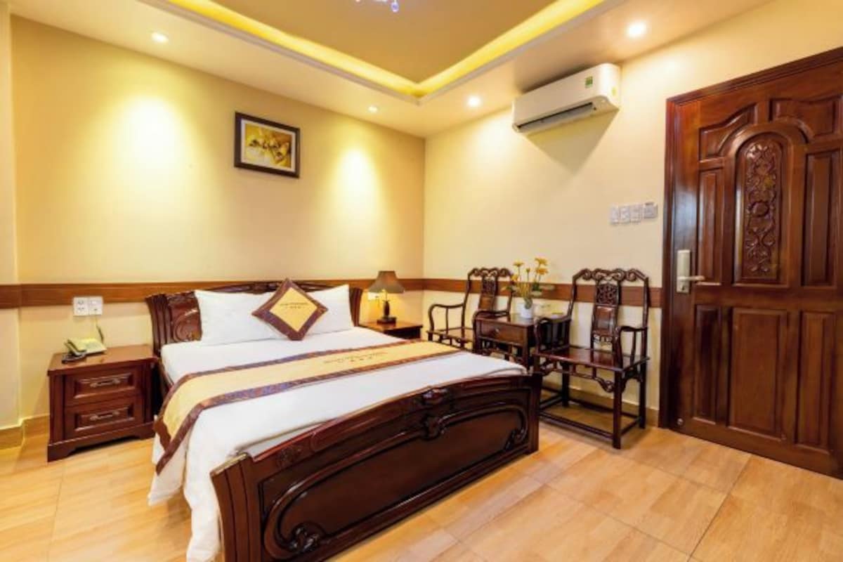 A hotel room with a wooden bed, bedside tables, a desk with chairs, and a wardrobe.