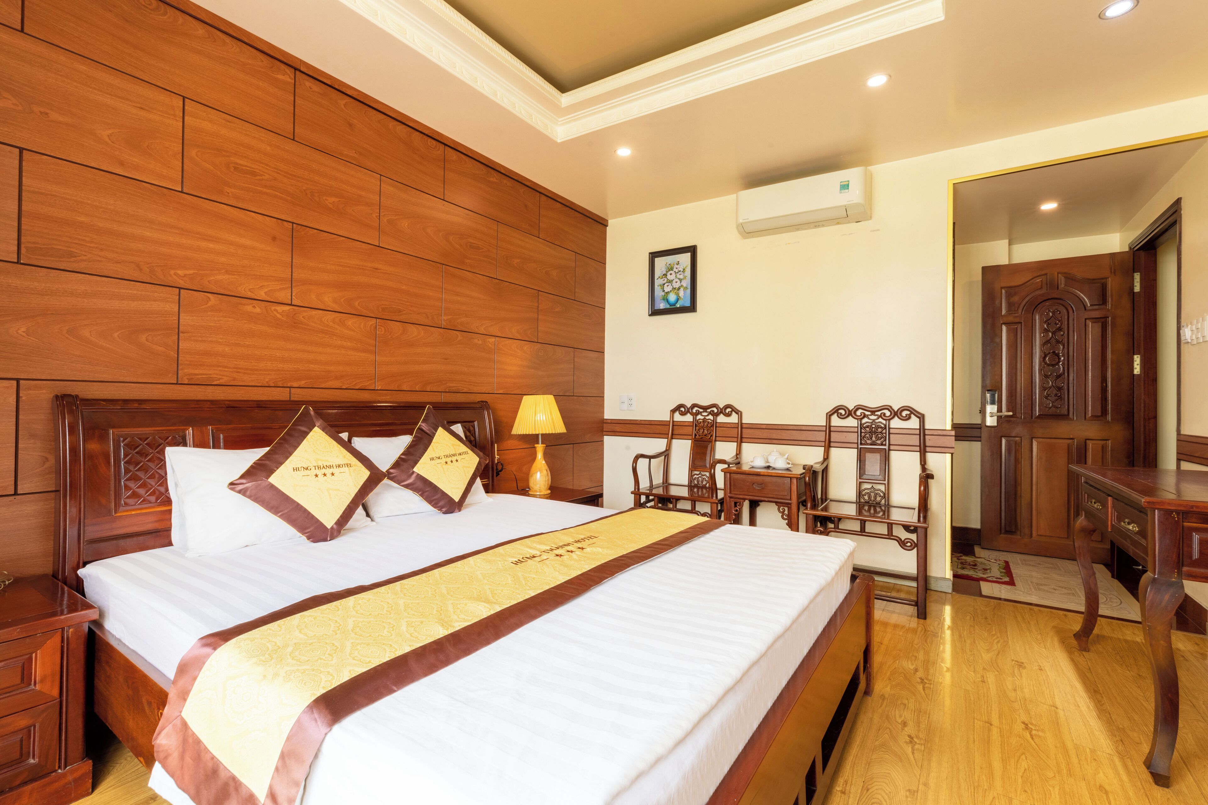 A hotel room with a large bed, wooden headboard, a bedside table, a nightstand, a desk, and a chair.