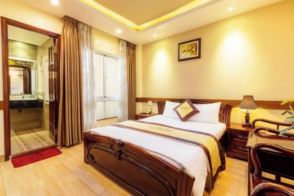 A hotel room with a large bed, a desk with a chair, a nightstand, and a door leading to a bathroom.