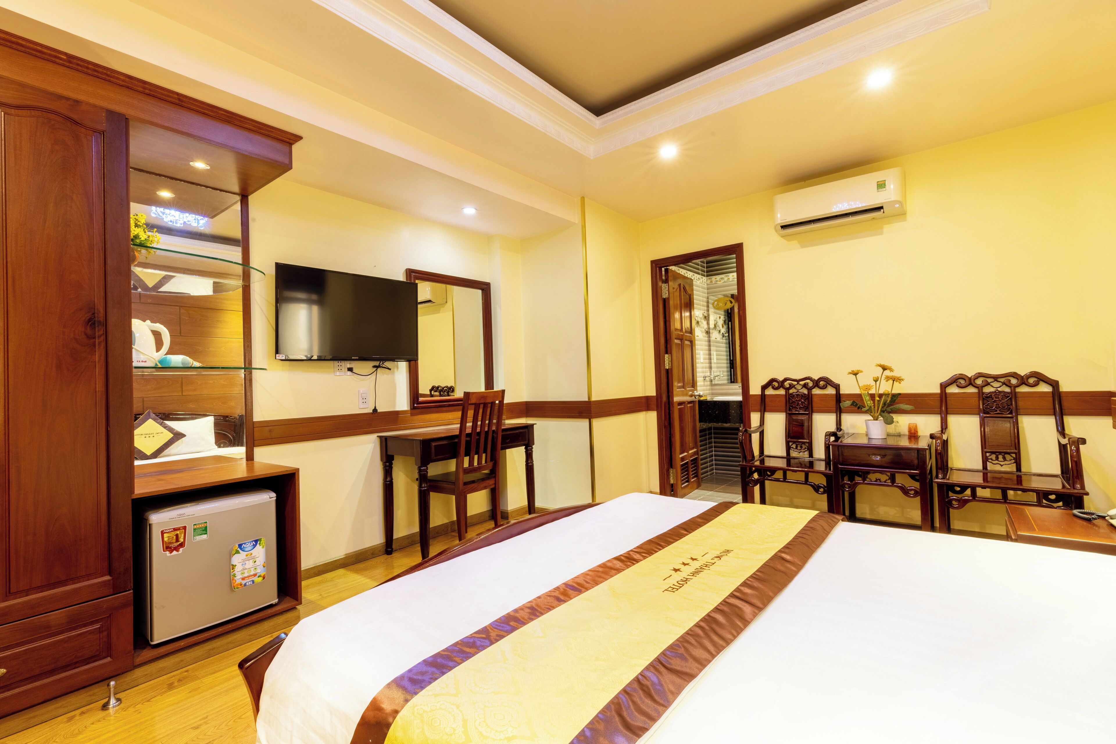 A hotel room with a bed, desk, chair, and a small refrigerator.