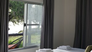 A bedroom with a large window, a bed with white linens, a nightstand, and a chair outside. - Farm Hoheheim (Windhoek Rural)