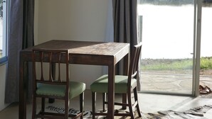 A dining area with a wooden table and chairs, a hanging light fixture, and a view of a body of water through a glass door. - Farm Hoheheim (Windhoek Rural)