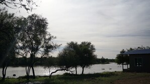 A lakeside view with trees and a small building. - Farm Hoheheim (Windhoek Rural)