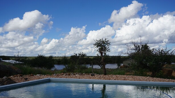 A swimming pool with a clear view of the surrounding landscape, including a body of water and trees. - Farm Hoheheim (Windhoek Rural)