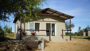 A single-story house with a stone wall in front, a bench, and a patio area. - Farm Hoheheim (Windhoek Rural)