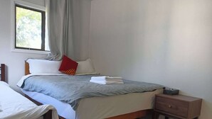 A bedroom with a bed, a nightstand, a window, and a view of trees. - 1 Bedroom garden chalet 7B  (Rotorua)