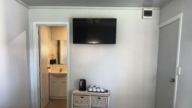 A hotel room with a bed, a TV mounted on the wall, a small kitchenette with a sink, and a microwave. - 1 Bedroom garden chalet 7B  (Rotorua)