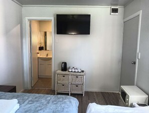 A hotel room with a bed, a TV mounted on the wall, a small kitchenette with a sink, and a microwave. - 1 Bedroom garden chalet 7B (Rotorua)
