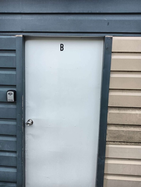 A white door with a 'B' marking, a doorbell, and a grey frame. - 1 Bedroom garden chalet 7B (Rotorua)